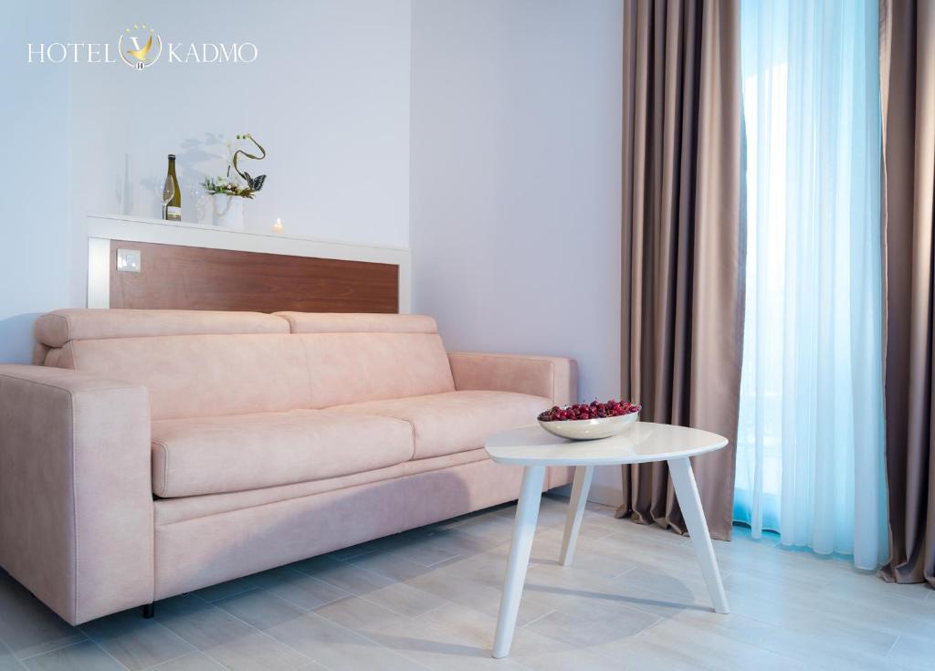 Mūsdienīgs viesnīcas numurs ar rozā dīvānu un baltu galdiņu, uz kura ir augļu bļoda. Logi ar gaisīgām aizkariem ļauj dabīgajai gaismai iekļūt telpā.