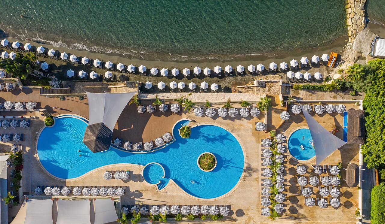 Vasaras kūrorta baseins ar saulessargiem un pludmali, redzams no augšas. Dzinējspēks relaksācijai un atpūtai pie ūdens. panoramic view with beach and pools