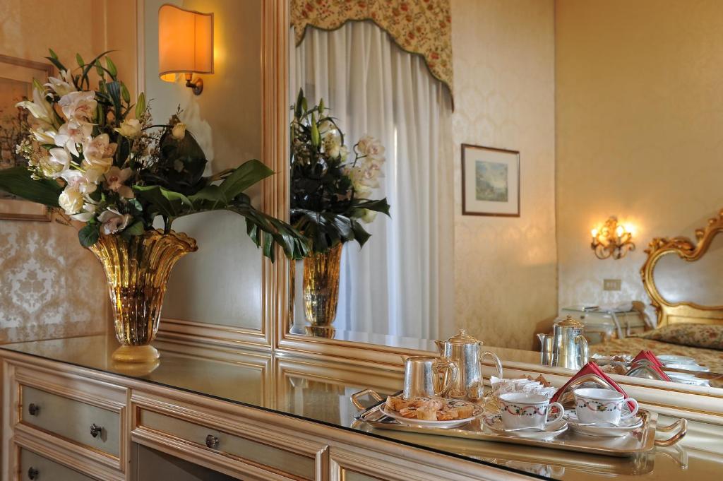 Greznas viesnīcas interjers ar ziedu kompozīciju un tējas servēšanu uz spoguļgalda. Eleganti dekorēta telpa ar gaišiem toņiem un izsmalcinātu mēbeļu dizainu.
