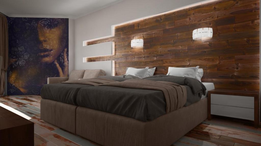 Mūsdienīga guļamistaba ar koka sienu un māksliniecisku fonu, kas attēlo seju. Gulta ir ērta, ar mīkstiem spilveniem un segu. Apgaismojums radīts ar modernām lampām.