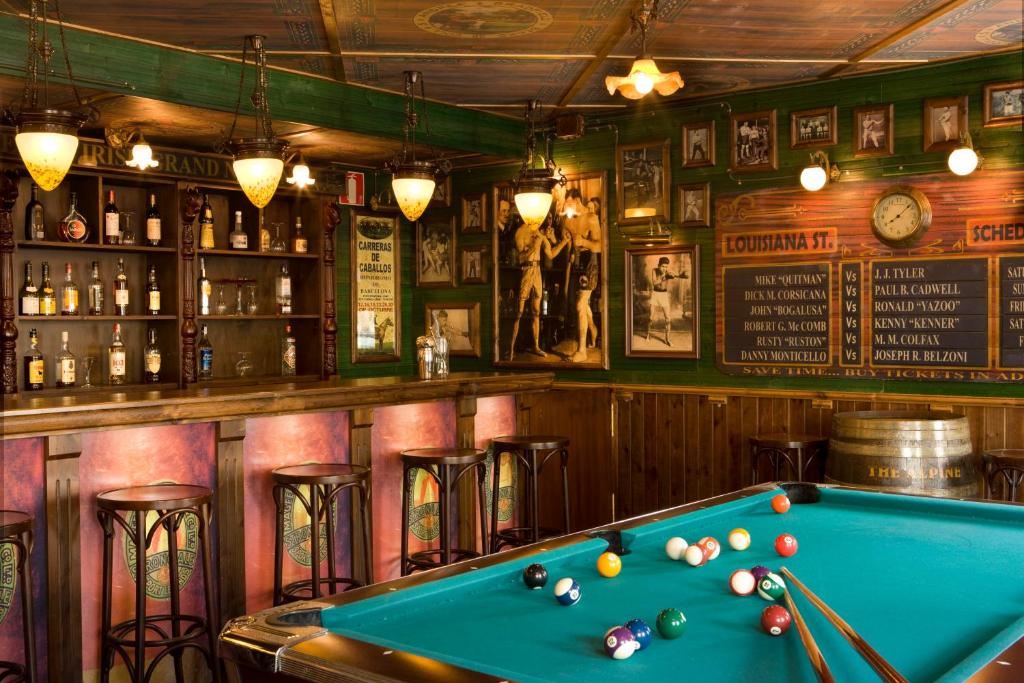 Bārs ar biljarda galdu, kurā pie sienām ir mākslas darbi un dažādas dzērienu pudeles. Apkārt ir koka krēsli un gaismas, radot siltu atmosfēru.