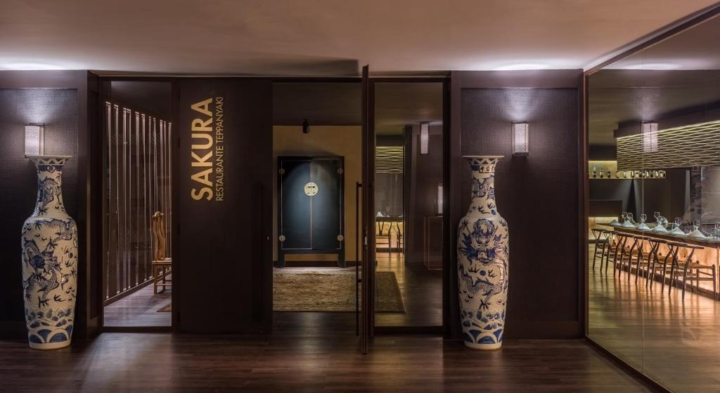 Eleganta restorāna ieeja ar nosaukumu "Sakura", kurā redzami izsmalcināti zili un baltā porcelāna vāzes. Interjers ir mūsdienīgs un silts, radot patīkamu atmosfēru.