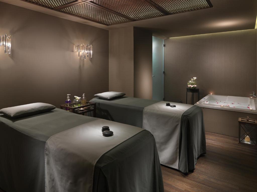 Relaksējoša spa istaba ar divām masāžas galdiem, greznām gaismām un burbuļvannu. Interjers ir veidots mierīgā un elegantā stilā, radot patīkamu atmosfēru atpūtai.