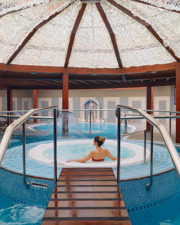Luksusa spa vidē, kur sieviete atpūšas burbuļvannā zem grezna dekoratīva jumta. Svaiga un relaksējoša atmosfēra aicina uz mierīgu brīdi.