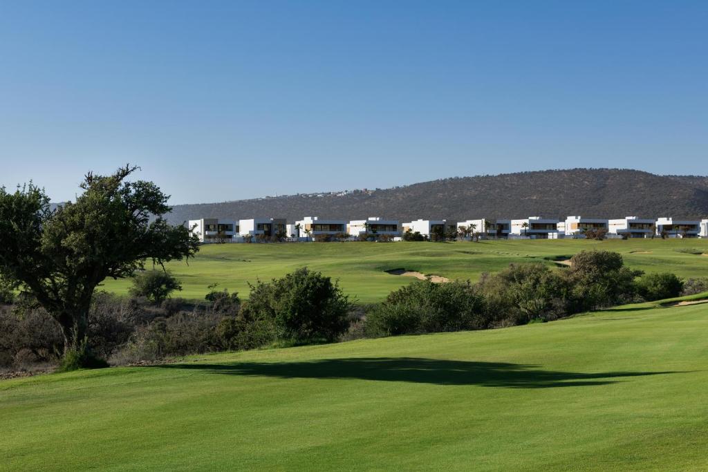 Lieliska ainava ar golfa laukumu un modernām mājām kalnu fona. Zaļā zāle un zilo debesu skats rada mierīgu atmosfēru.
