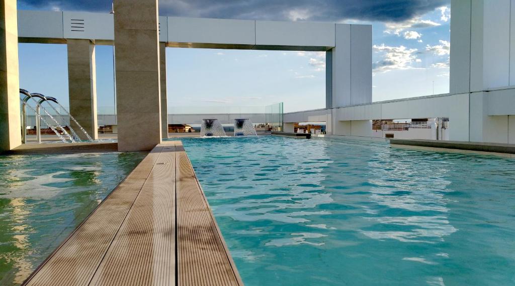 Peldbaseins ar skatu uz debesis, moderns dizains un koka terase, kas rada relaksējošu atmosfēru. Ūdens strūklakas pievieno eleganci šai atpūtas vietai.