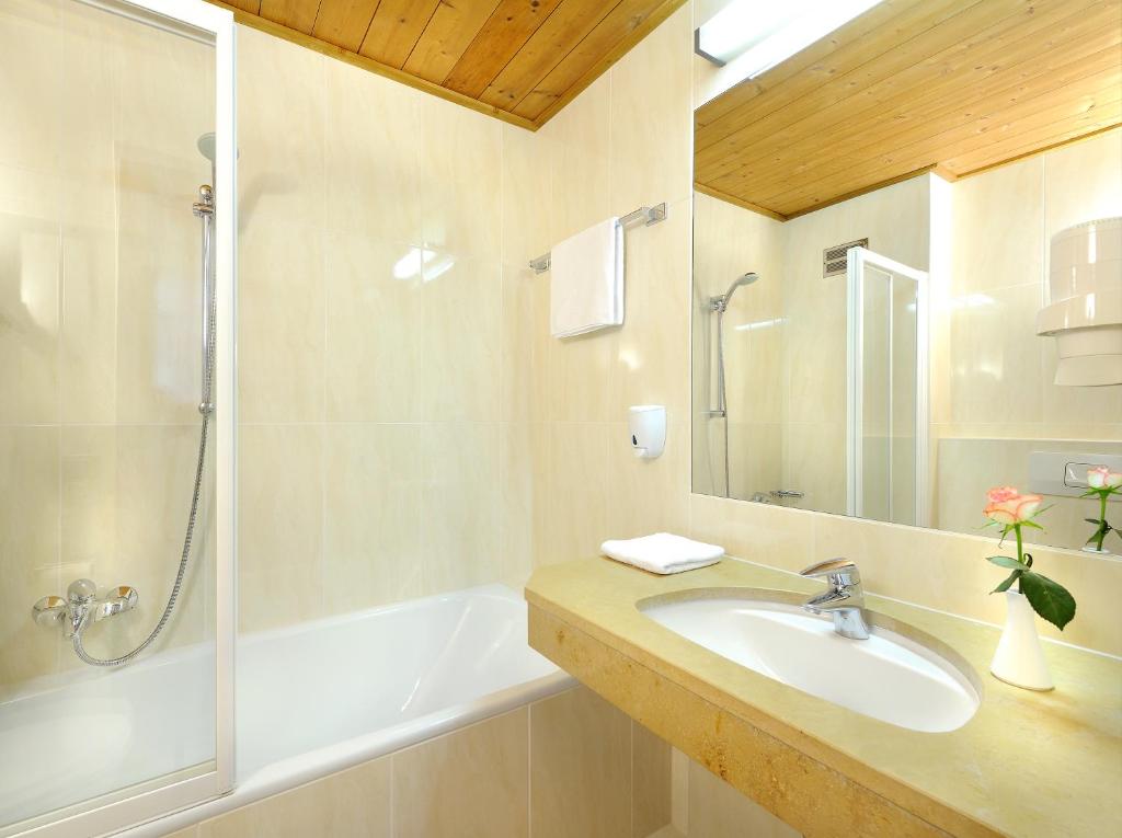 Mūsdienīgs vannas istabas interjers ar dušu, vannu un izsmalcinātu izskatu, papildināts ar ziediem uz izlietnes.