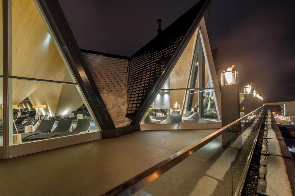 Mūsdienīga arhitektūra ar asām līnijām un lieliem logiem, kas piedāvā skatu uz interjeru. Nakts apgaismojums rada siltu un aicinošu atmosfēru.