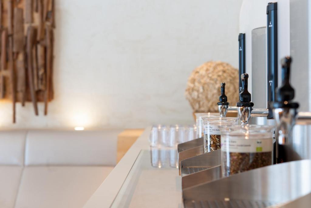 Bāra lete ar vairākiem dzērienu krāniem un stikla traukiem, kas satur dažādas sastāvdaļas. Fons ir gaišs ar dekoratīviem elementiem.