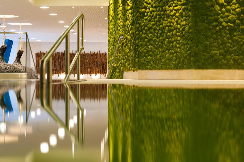 Mūsdienīgs interjers ar zaļo sūnu sienu un atspīdumu ūdenī, radot relaksējošu atmosfēru. Dekoratīvie elementi un apgaismojums piešķir telpai eleganci.