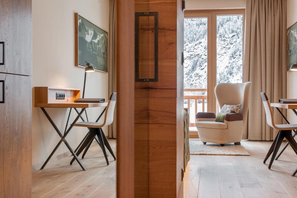 Mūsdienīgs viesnīcas numurs ar koka detaļām, rakstāmgaldu un ērtu atpūtas krēslu, kas piedāvā skatu uz sniegotām kalnu ainavām.