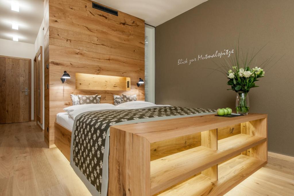 Mūsdienīga guļamistaba ar koka apdari un siltu apgaismojumu, kurā redzams gultas komplekts un dekoratīvās detaļas. Uz galda ir ziedi un āboli, radot mājīgu atmosfēru.