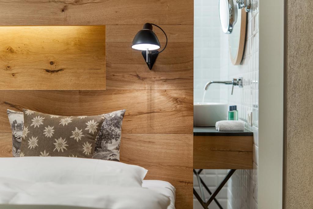 Mūsdienīgs guļamistabas interjers ar koka sienu un spilvenu, kas rotāts ar ziedu rakstu. Redzama arī vannas istaba ar modernu izskatu un vannas piederumiem.