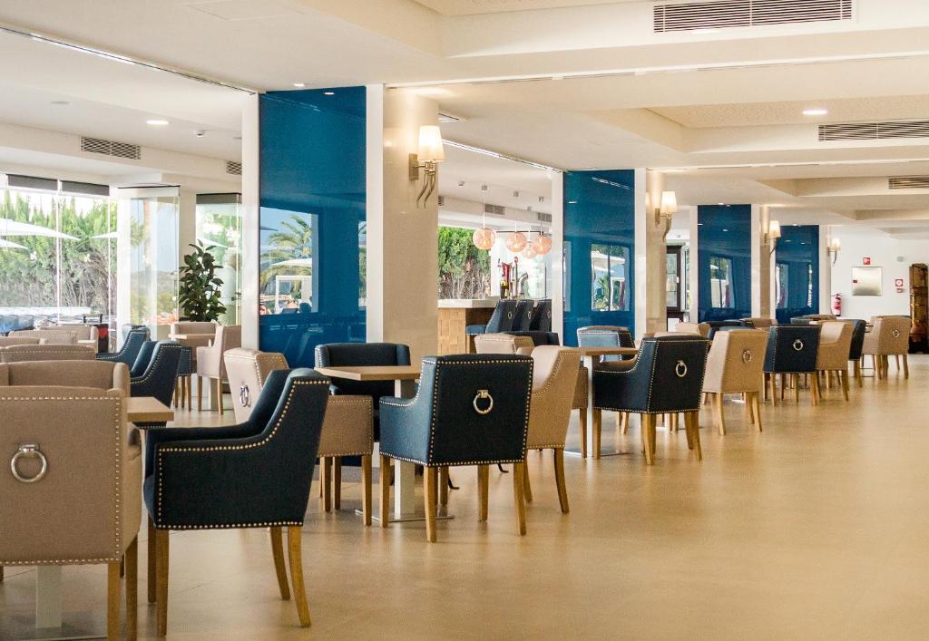 Mūsdienīga restorāna interjers ar ērtiem krēsliem un lieliem logiem, kas nodrošina dabisko apgaismojumu. Eleganta, atvērta telpa ar gaišām krāsām un stilīgu dizainu.