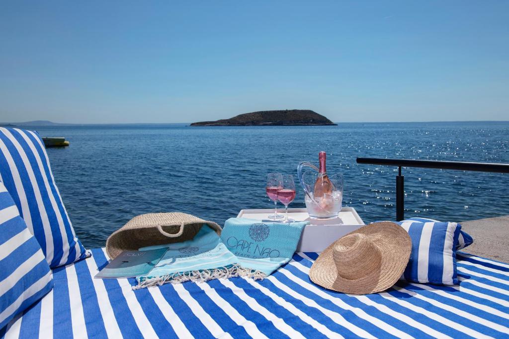 Atpūtas vieta pie jūras ar zilo un baltu svītru sauļošanās krēslu, rozā vīnu un saules cepuri, kas rada relaksējošu atmosfēru. Ideāla vieta vasaras brīvdienām.