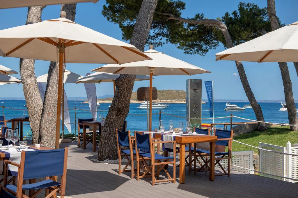 Restorāna terase ar skatu uz jūru, kur koka galdi un krēsli ir izvietoti zem lieliem saules jumtiem, nodrošinot ērtu un relaksējošu atmosfēru. Ideāla vieta, lai izbaudītu maltīti ar skatu uz ūdeni.