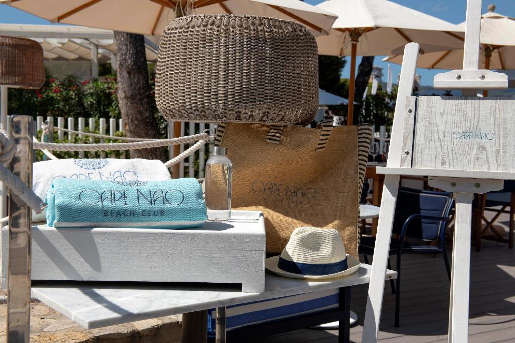 Alt teksts: Pludmales kluba aksesuāri, tostarp dvieli, somiņa un cepure, izvietoti saulainā vidē ar ēnām no lietussargiem.