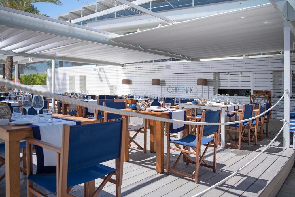 Āra restorāns ar elegantiem galdiem un krēsliem, kas izvietoti zem nojumes, radot relaksējošu atmosfēru. Ideāla vieta, lai baudītu maltīti brīvā dabā.