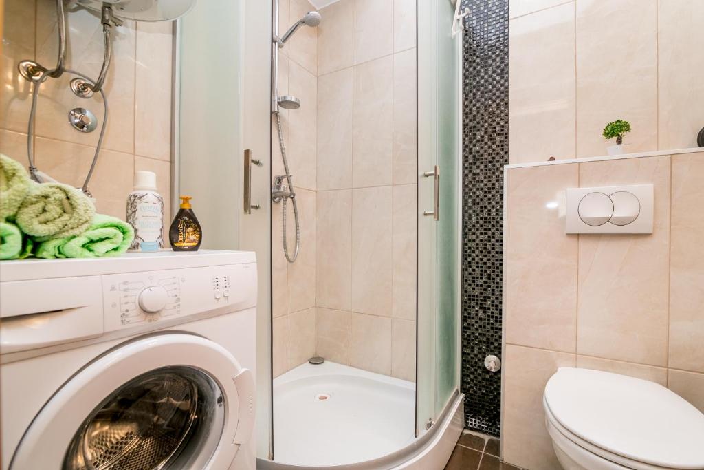 Mūsdienīga vannas istaba ar stikla dušu, veļas mašīnu un zaļām dvieļiem, pievienojot elegantu dizainu un praktiskus elementus.