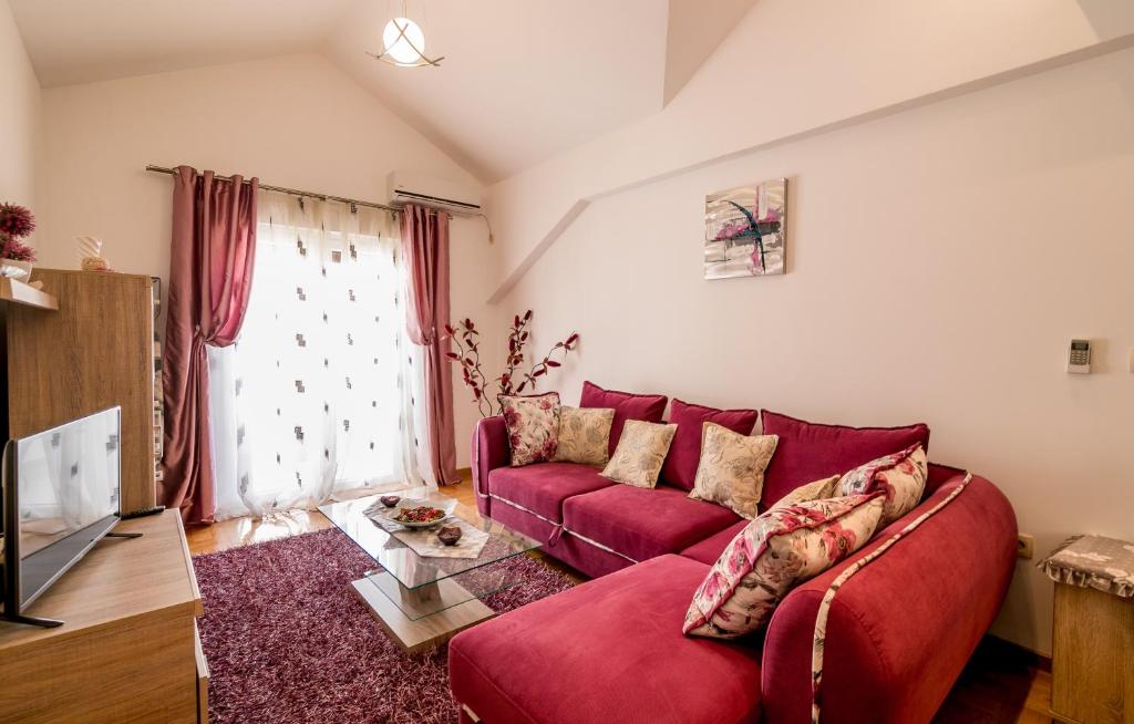 Mūsdienīgs dzīvojamās istabas interjers ar sarkaniem dīvāniem, glāzēm uz galda un gaišiem aizkariem, kas ielaiž dabisko gaismu. Eleganta dekorācija un mājīga atmosfēra.