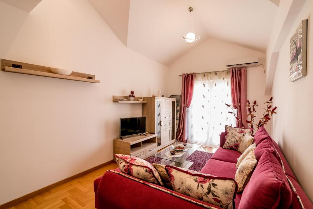 Mūsdienīgs viesistabas interjers ar sarkanu dīvānu, televizoru un gaišām aizkariem, radot mājīgu atmosfēru. Iekārtota ar dekoratīviem elementiem un dabīgām krāsām.