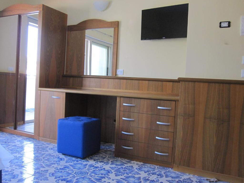 Mūsdienīga guļamistaba ar koka mēbelēm, spoguli un televizoru uz sienas, kā arī zilu pufu. Flīžu grīda ar rakstu.