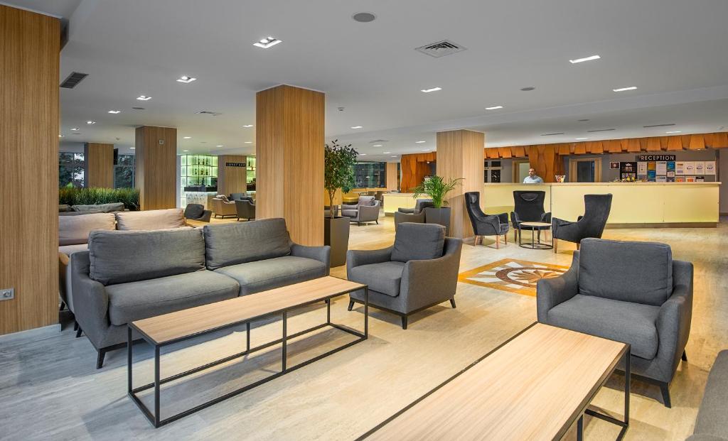 Mūsdienīgs viesnīcas hols ar ērtiem dīvāniem un galdiem, kas aicina atpūsties un socializēties. Siltas krāsas un plašs telpas izkārtojums rada patīkamu atmosfēru.