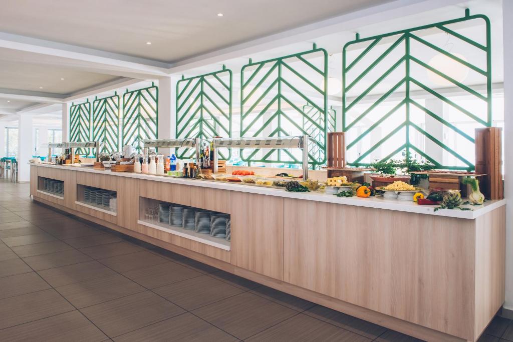 Mūsdienīga bufetes zona ar zaļām dekoratīvām restēm un plašu dārzeņu un ēdienu izvēli. Gaisīga atmosfēra ar dabīgiem materiāliem un ērtām sēdvietām.
