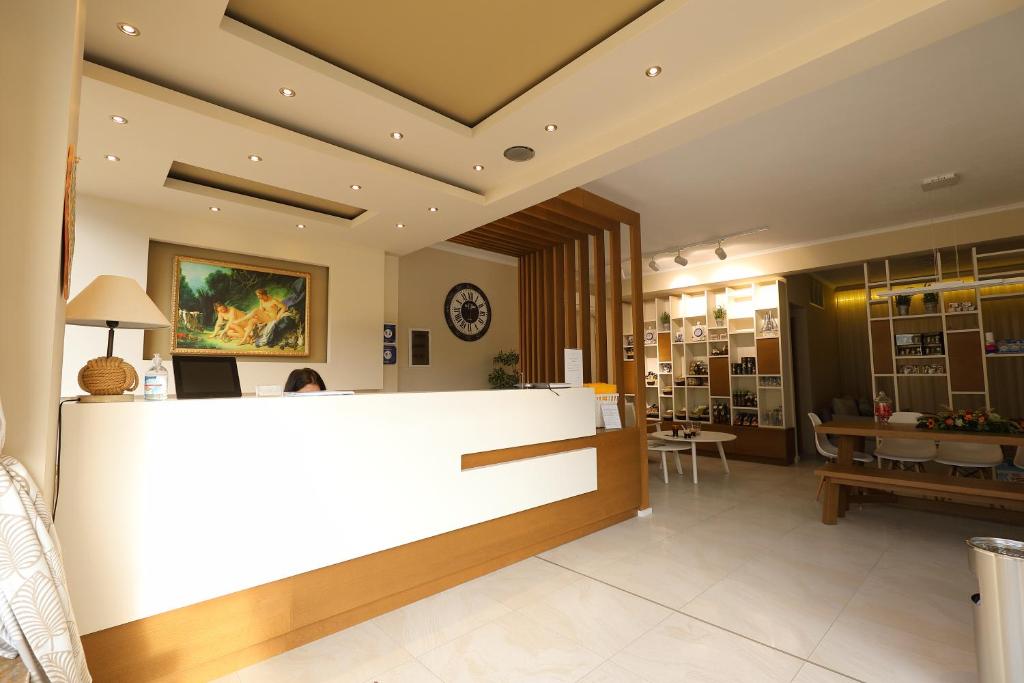 Mūsdienīgs reģistratūras interjers ar apgaismojumu, koka akcentiem un gleznu uz sienas, radot viesmīlīgu atmosfēru. Interjerā redzamas mēbeles un plaukti ar produktiem.