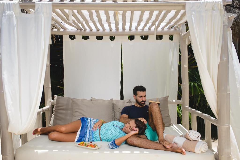 Pāris atpūšas zem teltī, baudot brīvdienu. Viņi atrodas ērtā gultā un blakus ir augļu šķīvis.