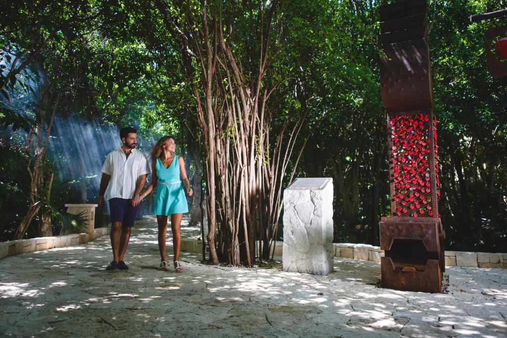 Pāris pastaigā gleznainā dabā, apņemti ar zaļumiem un saules stariem, blakus atrodas māksliniecisks objekts ar ziediem.