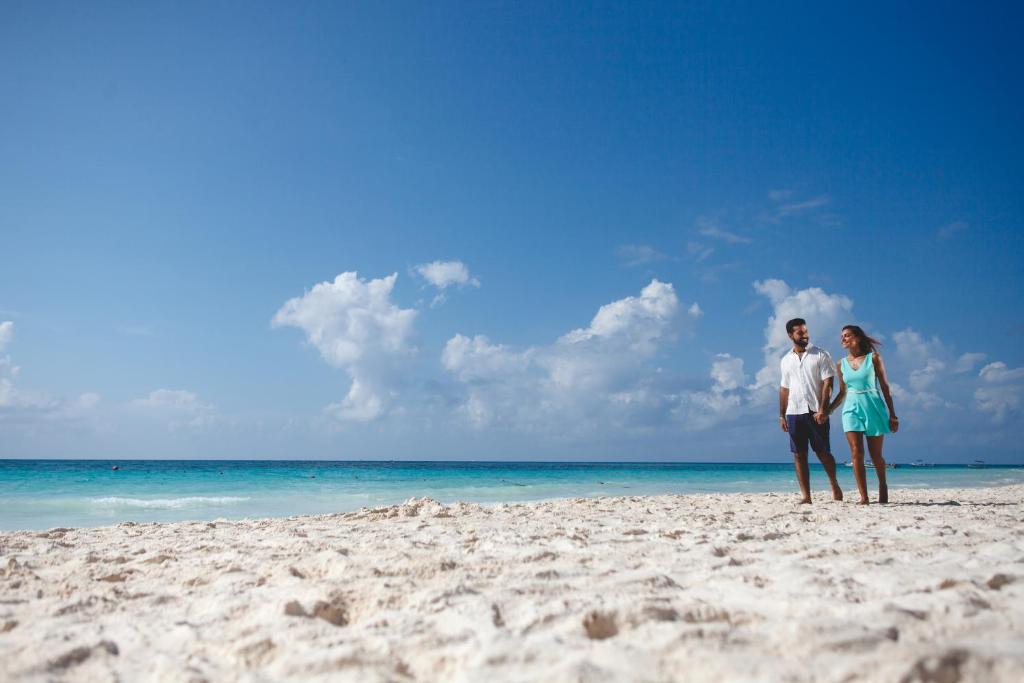 Jauna pāra romantiska pastaiga pa pludmali, saulainā dienā ar skaidru zilo debesi un smilšainu krastu.