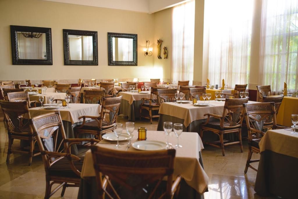 Elegants restorāna interjers ar koka mēbelēm un gaismas logiem, kas rada patīkamu atmosfēru. Galdi ir klāti ar galdautiem, un uz tiem ir glāzes un šķīvji.