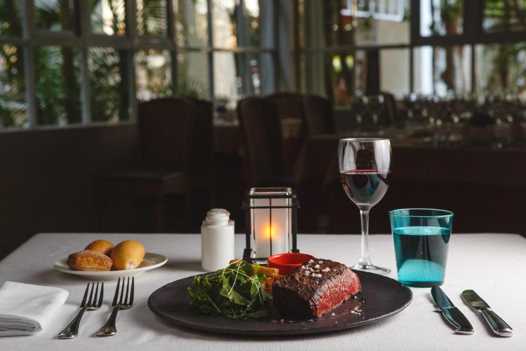 Elegants galda klājums ar gaļas ēdienu, salātiem un vīna glāzi, apgaismojums un restorāna atmosfēra. Ideāla vakariņu iedvesma.