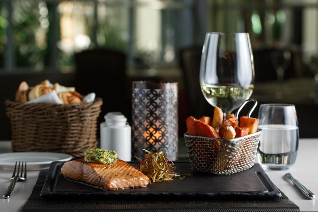 Smalki vakariņu galds ar ceptu lasi, garnējumu un ceptām kartupeļu šķēlītēm, papildināts ar glāzi balto vīnu un maizes grozu.