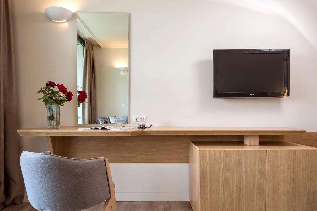 Mūsdienīgs viesnīcas numurs ar koka rakstu galdu, televizoru un ziediem vāzē, radot patīkamu un viesmīlīgu atmosfēru.