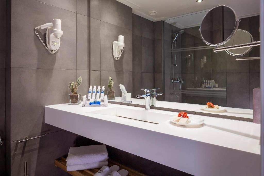 Mūsdienīgs vannas istabas interjers ar pelēkām flīzēm, baltu izlietni un spoguļiem, kas papildināts ar dekoratīviem elementiem, piemēram, kaktusiem un ziediem.