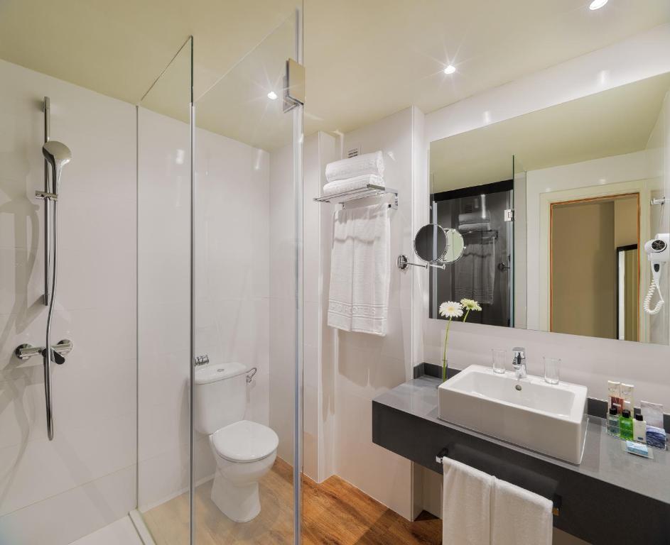 Mūsdienīgs vannas istabas interjers ar stikla dušu, tualeti un elegantu izlietni, papildināts ar dvieļiem un higiēnas piederumiem.