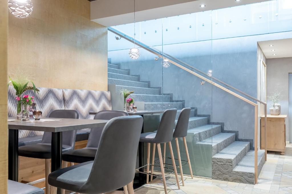 Mūsdienīgs interjers ar elegantām melnām krēslām un koka galdiem, kas izceļas ar vieglu atmosfēru un kāpnēm, kas ved uz augstāku stāvu. Ziedi uz galdiem piešķir dzīvīgumu.