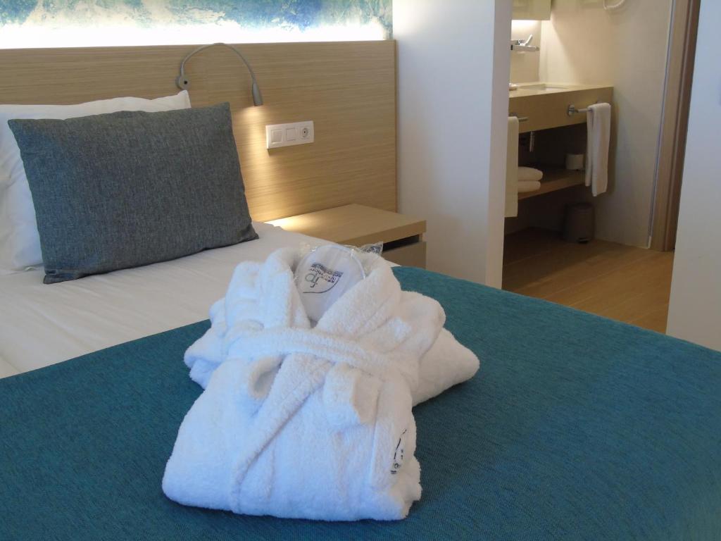 Mūsdienīga viesnīcas numura iekārtojums ar baltu halātu uz gultas, gaišu gultasveļu un skatu uz vannas istabu. Ideāla vieta atpūtai un komfortam.