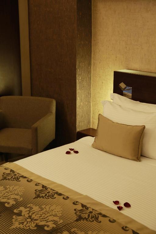 Mūsdienīgs guļamistabas interjers ar elegantu gultu, dekorētu ar rožu ziedlapiņām, un ērta krēsla stūrī. Siltas krāsas un grezni materiāli rada romantisku atmosfēru.