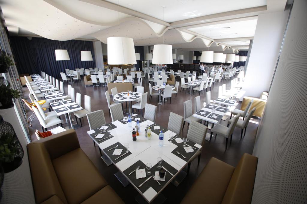 Liela un moderna restorāna telpa ar baltiem galdiem un krēsliem, kas sagatavoti viesiem. Gaisma un mūsdienīga dekorācija rada patīkamu atmosfēru.