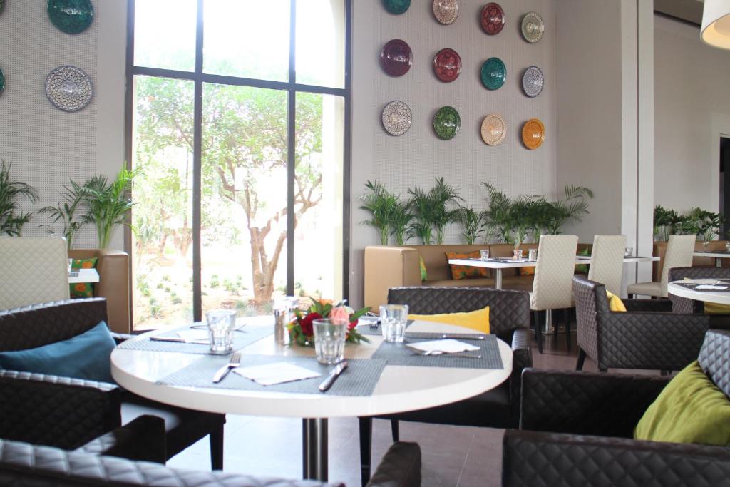 Mūsdienīgs restorāna interjers ar komfortablām krēslām un elegantiem galdiem, dekorēts ar krāsainām plāksnēm uz sienas un zaļām augu rotājumiem. Gaisīgs un viesmīlīgs atmosfēra, ideāla vieta maltītēm.