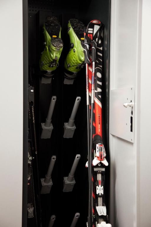 Slēpju skapī redzami zaļi slēpošanas zābaki un divi slēpes ar sarkaniem un melniem akcentiem. Skapī ir nodrošināta vieta zābakiem un slēpēm, kas ir sakārtotas kārtīgi un ērti.