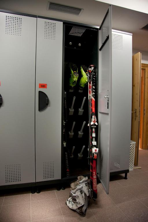 Ski equipment is stored in a grey locker, featuring bright green ski boots and a pair of skis leaning against it.