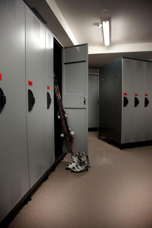 Slēpošanas skapīši ar atvērtu durvīm un slēpēm, kas novietotas uz grīdas. Telpa ir labi apgaismota un tīra.