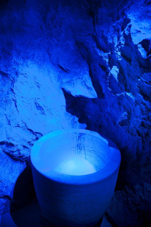 Zilā gaismā apgaismots akmens sienas fons ar apaļu, gaišu trauku, kas atrodas priekšplānā.