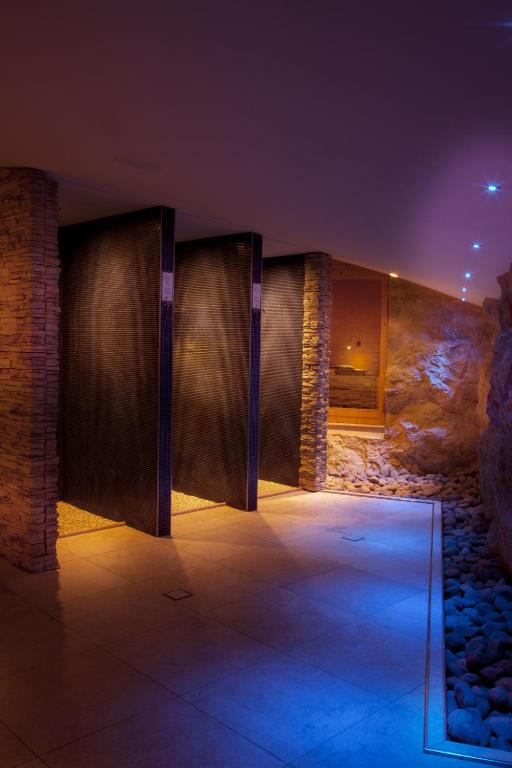 Mūsdienīga spa telpa ar akmens sienām un relaksējošu apgaismojumu, kurā redzami dušu kabīnes un akmeņi. Ideāla vide atpūtai un relaksācijai.