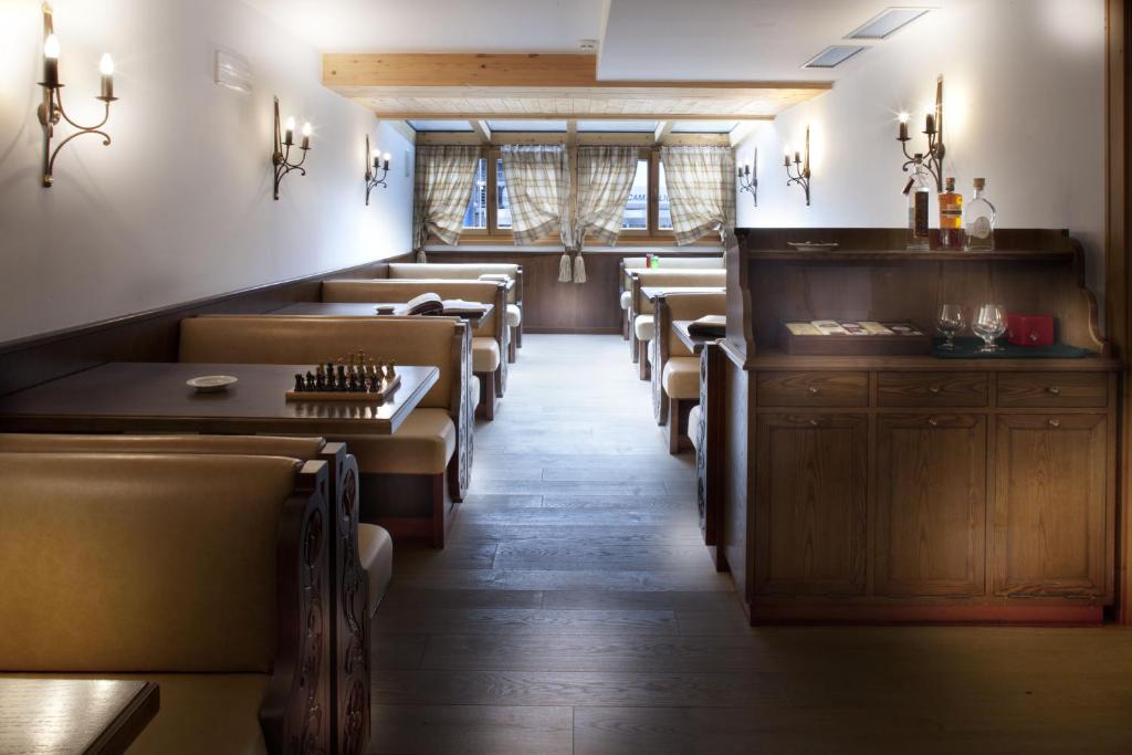 Restorāna interjers ar koka mēbelēm, šokolādes krāsas sēdekļiem un elegantiem gaismas ķermeņiem, radot siltu un viesmīlīgu atmosfēru. Logi ar aizkariem piedāvā skatu uz ārpusi, papildinot kopējo noskaņu.