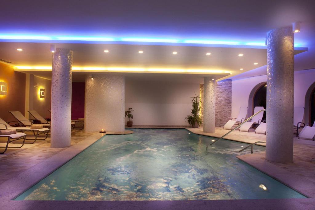 Mūsdienīgs iekštelpu baseins ar relaksējošu apgaismojumu un ērtām sauļošanās krēslām, radot mierīgu un lētu atmosfēru.